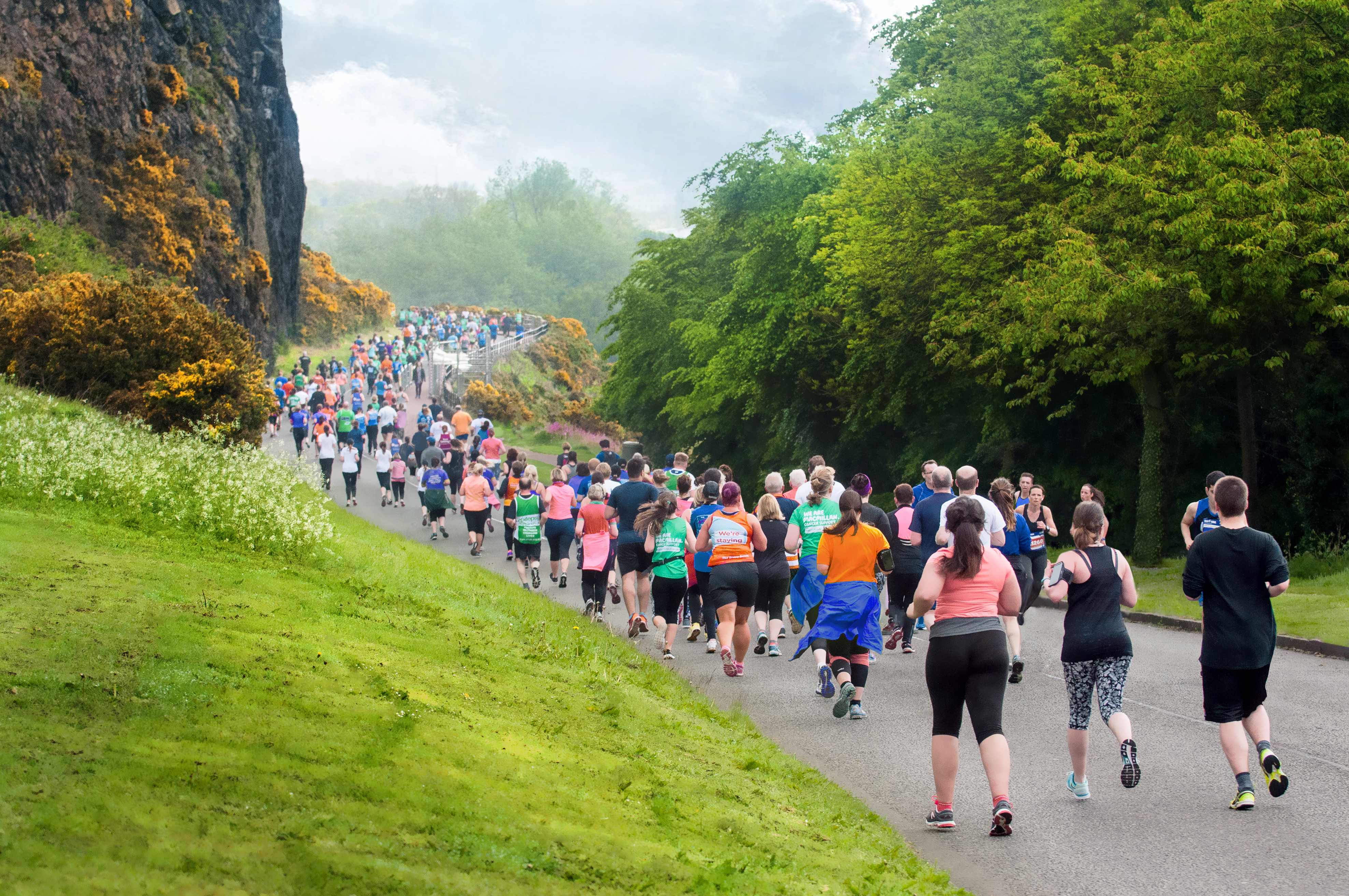 Back view of many runners running along a scenic, foggy mountain edge in Edinburgh.