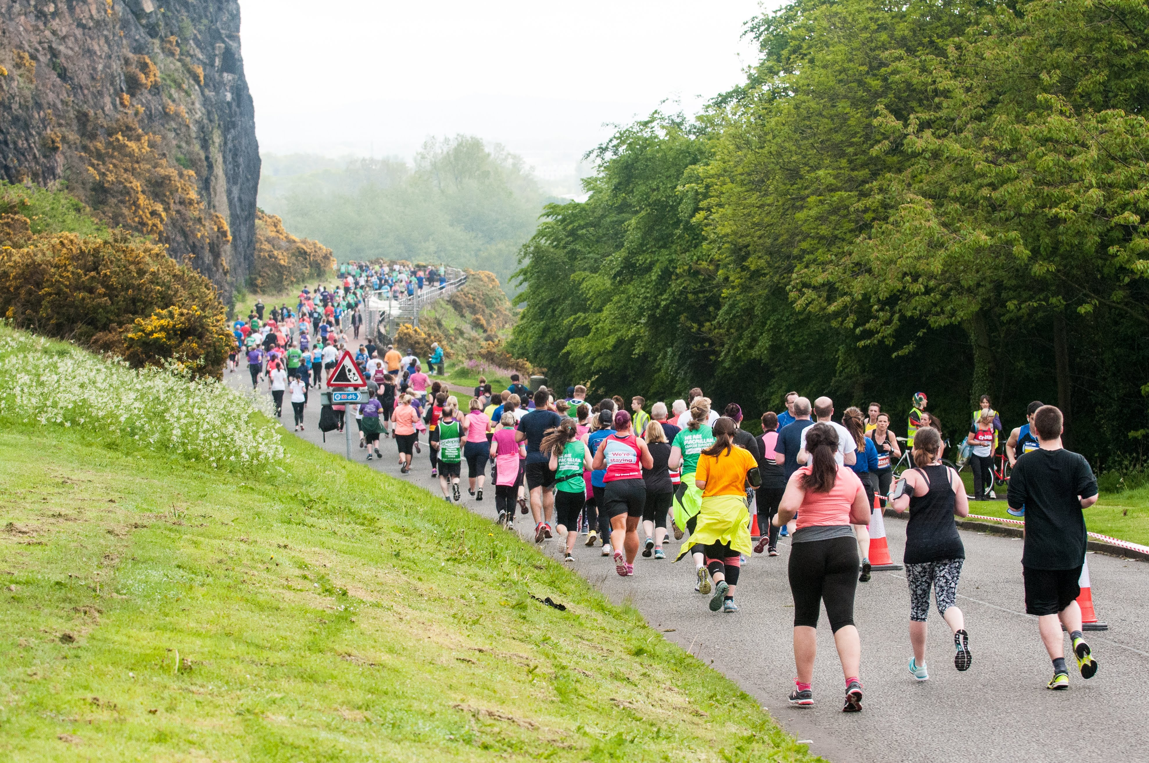 Back view of many runners running along a scenic, foggy mountain edge in Edinburgh.