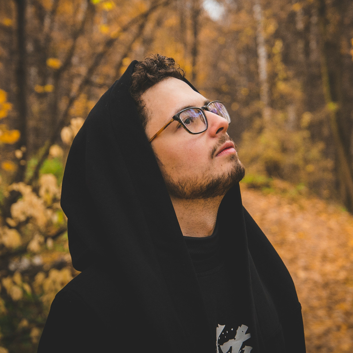 Young man with glasses in black clothes in an autumn forest looking upwards