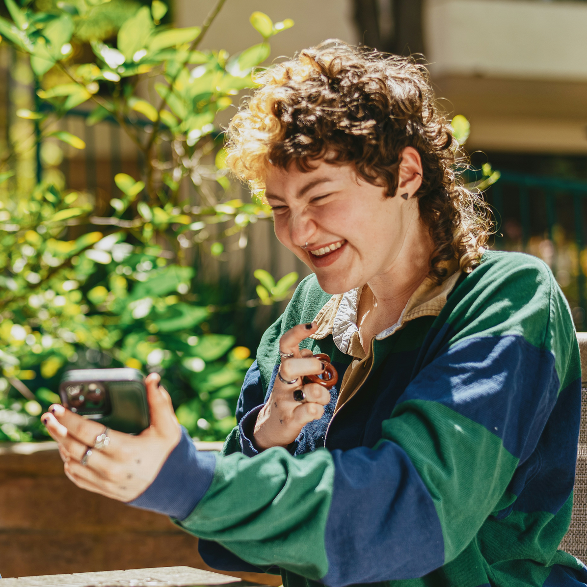 A young woman is sat down laughing at something funny on her phone