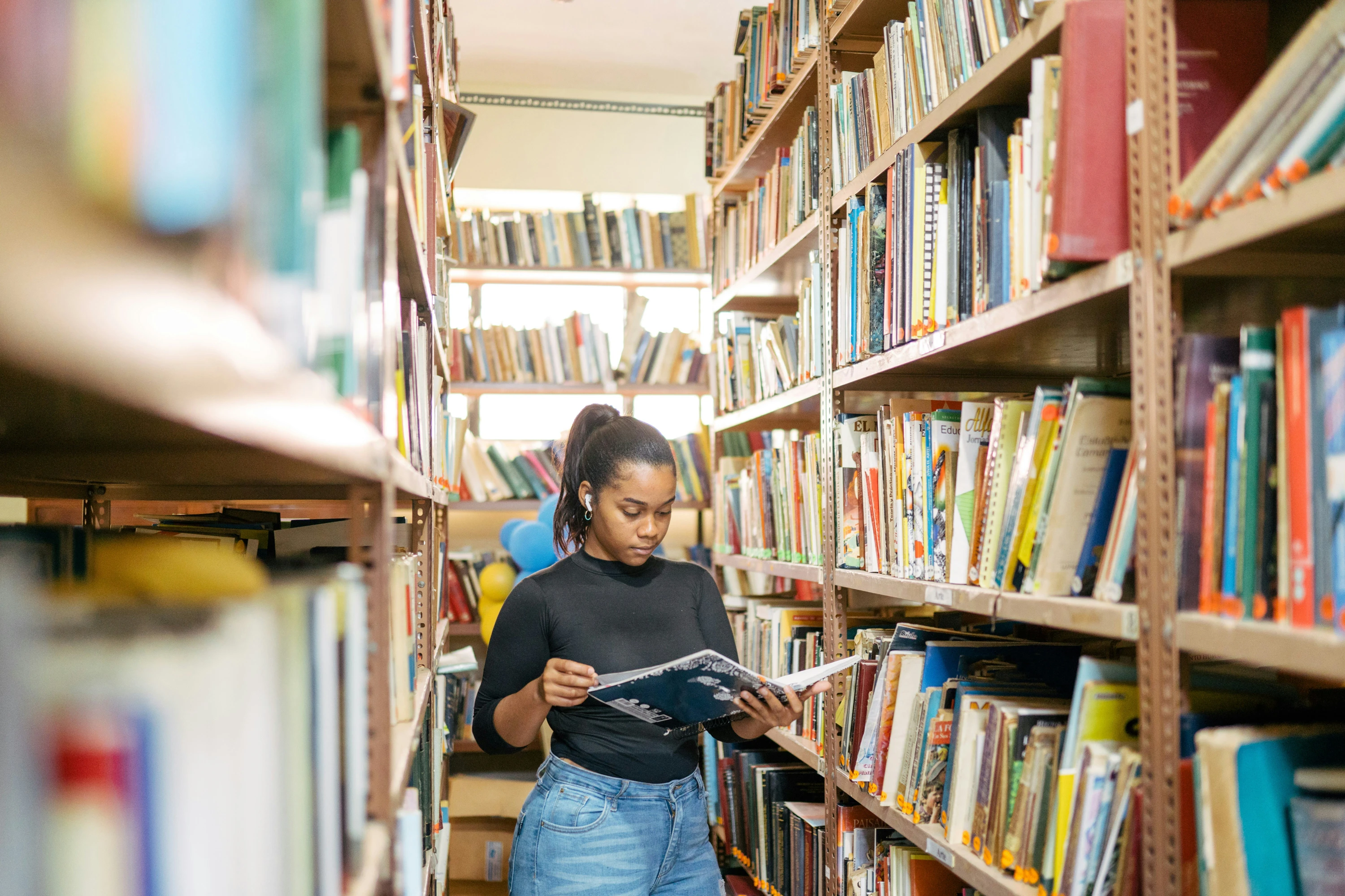 A young woman is reading a book in a library, shelves of books surround her