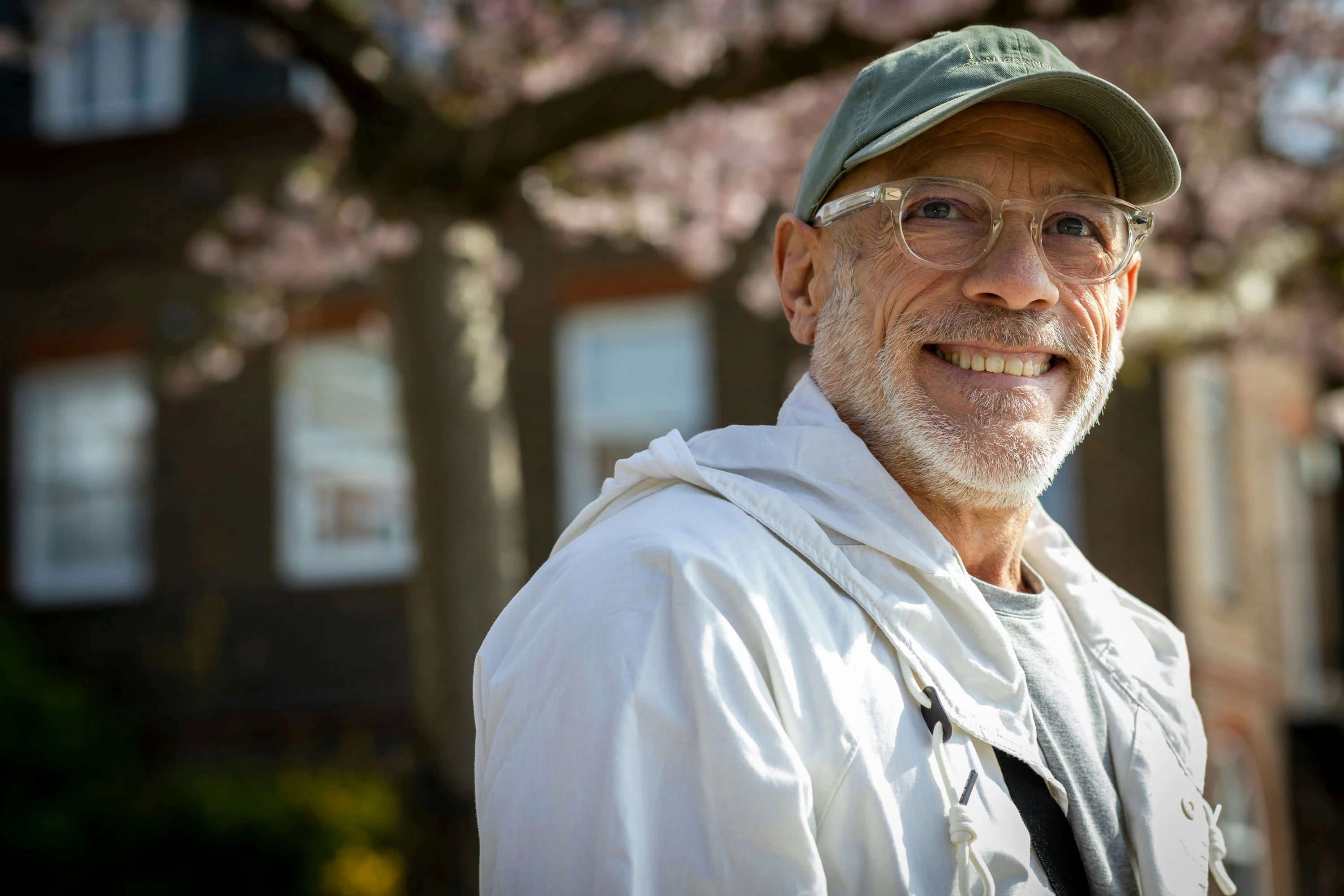 An older man wearing a hat and glasses standing outside