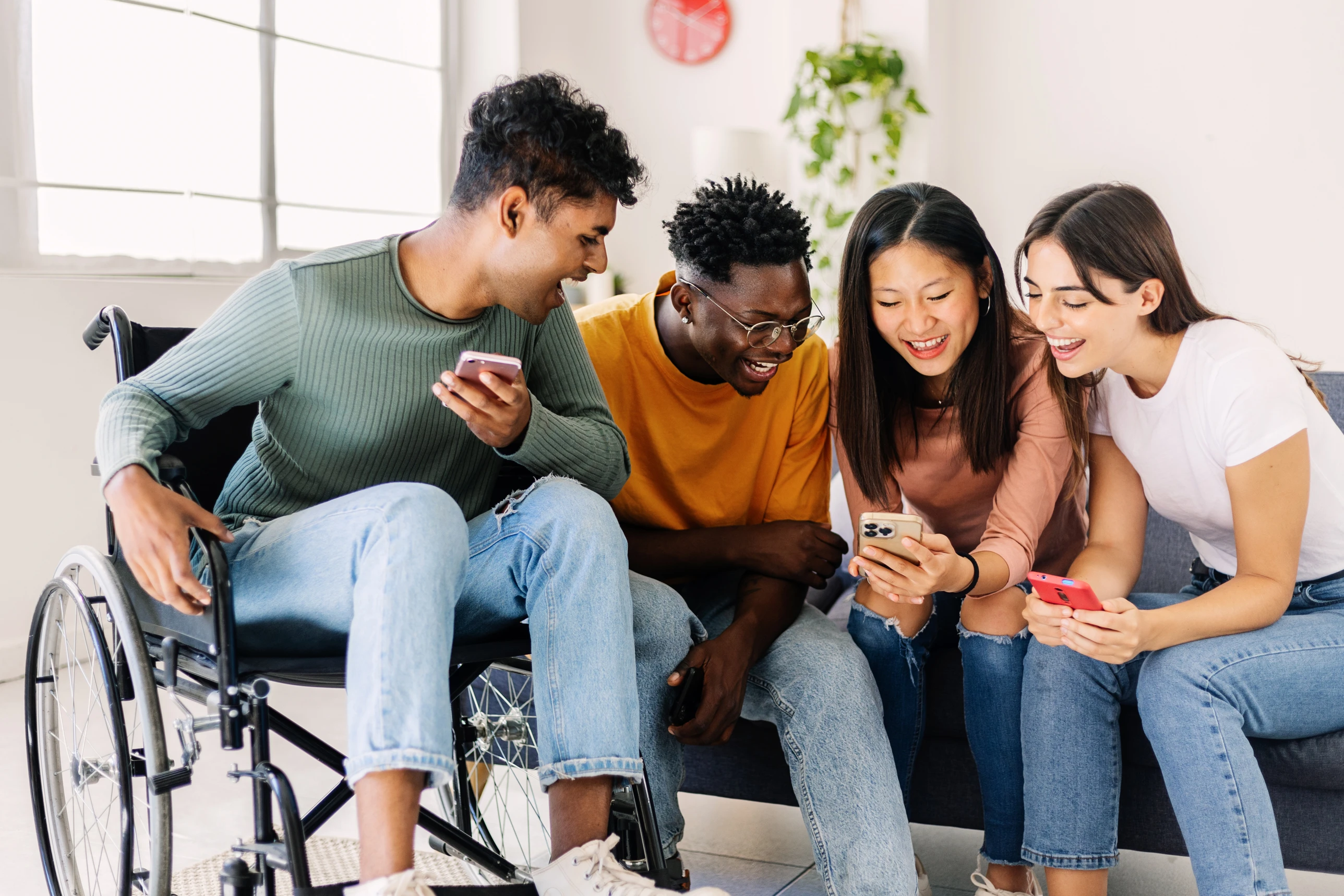 A group of friends are sat around smiling whilst looking at their phones