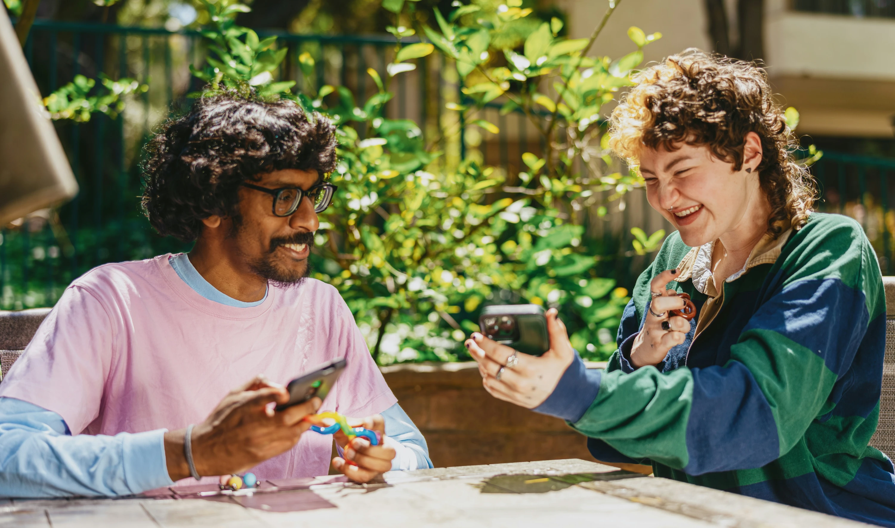 Two young people are sat down laughing and smiling whilst looking at something funny on their phone