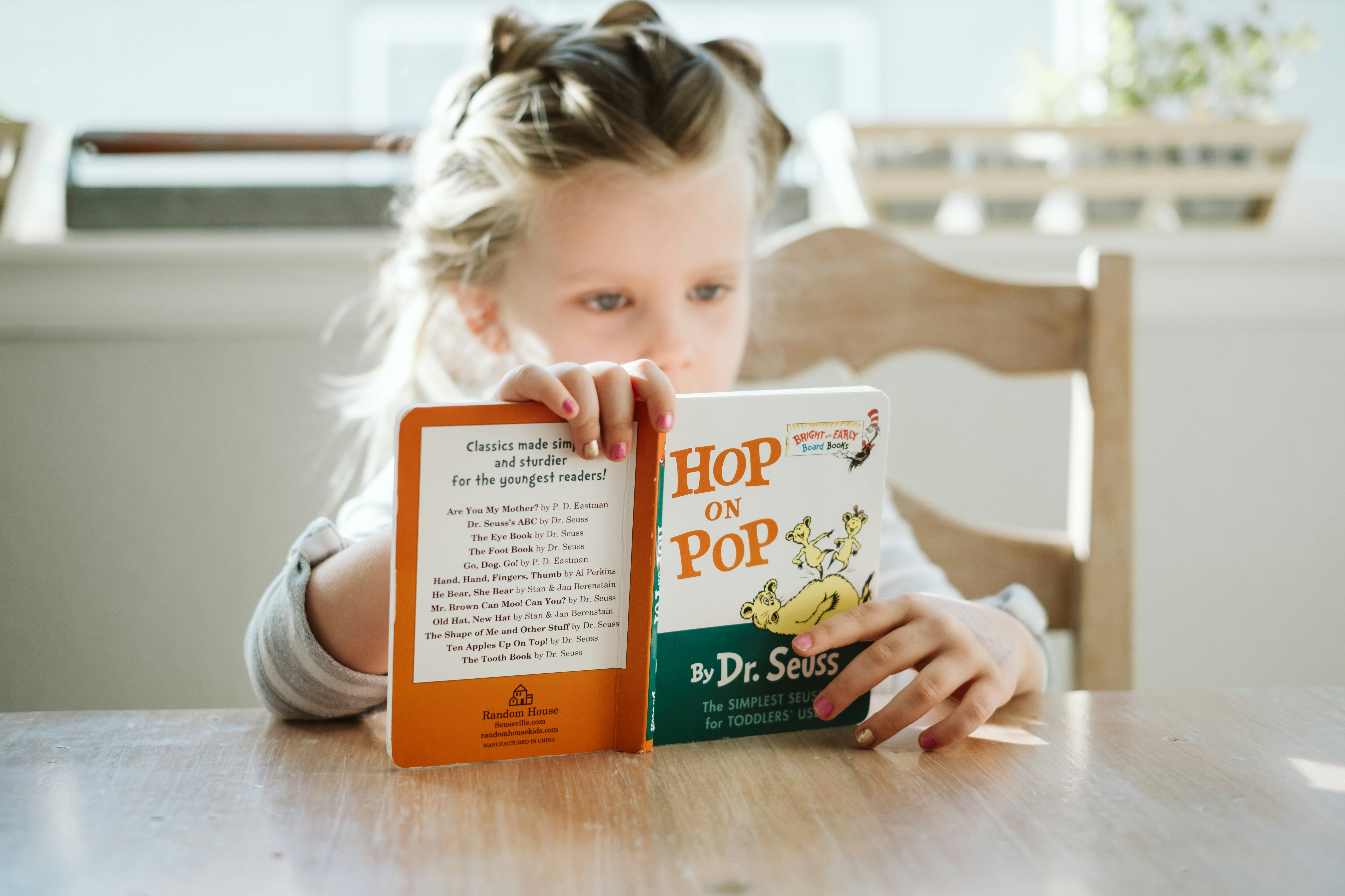 A young girl sitting at a table while reading a book