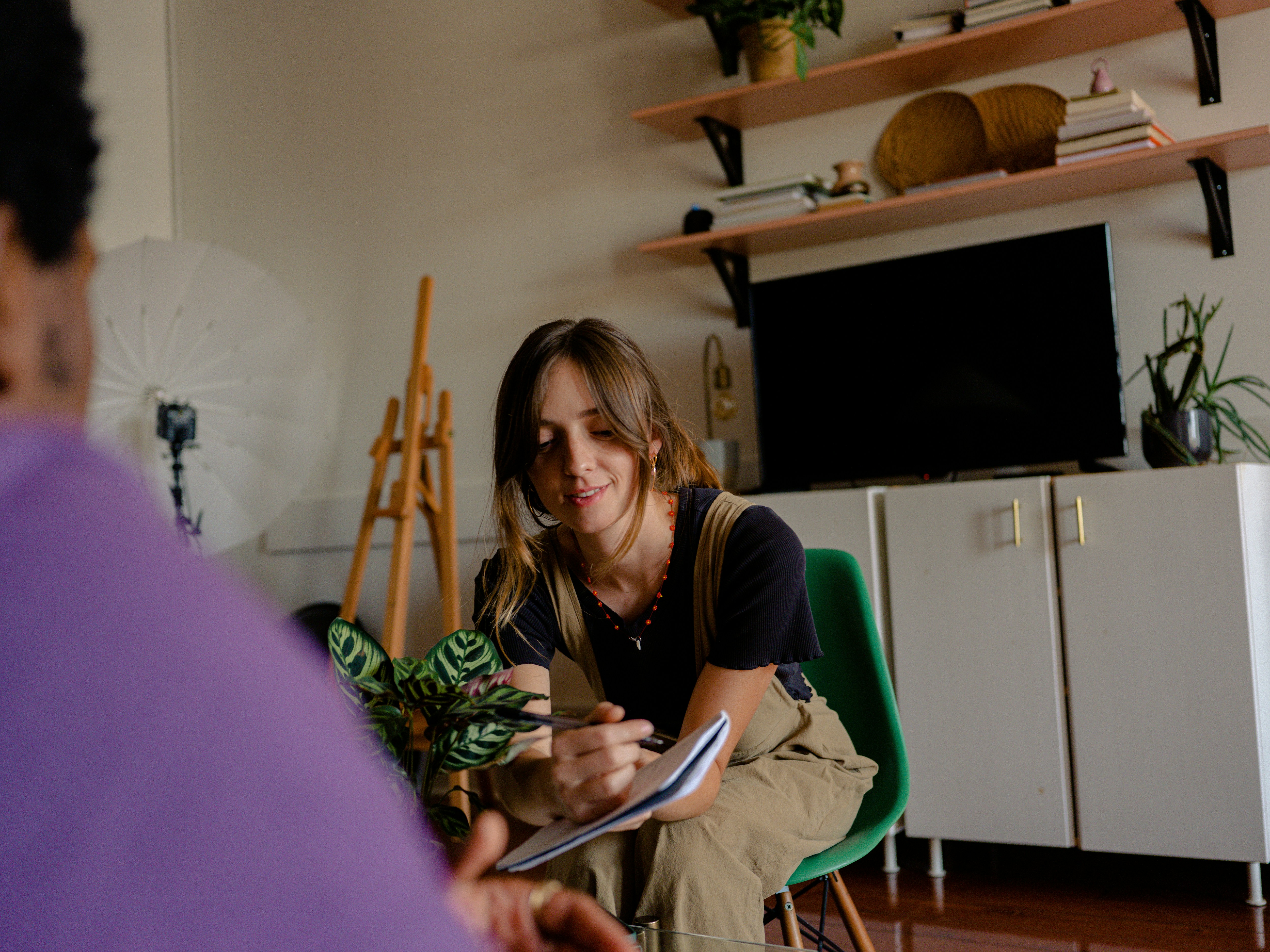 A woman sitting down writing on a piece of paper whilst talking to a man