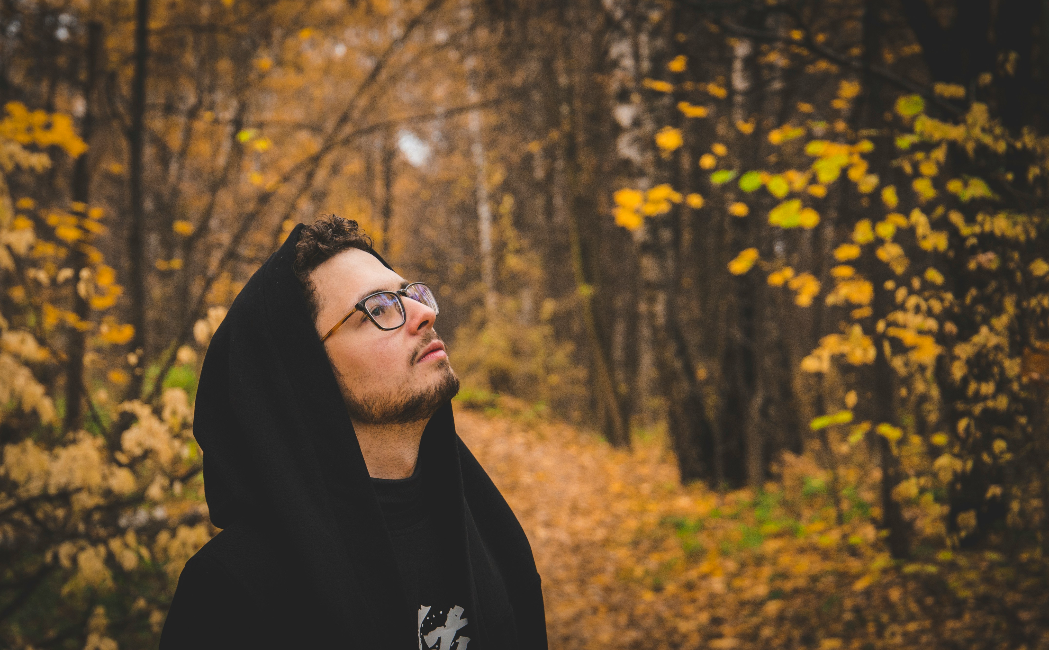 Young man with glasses in black clothes in an autumn forest looking upwards