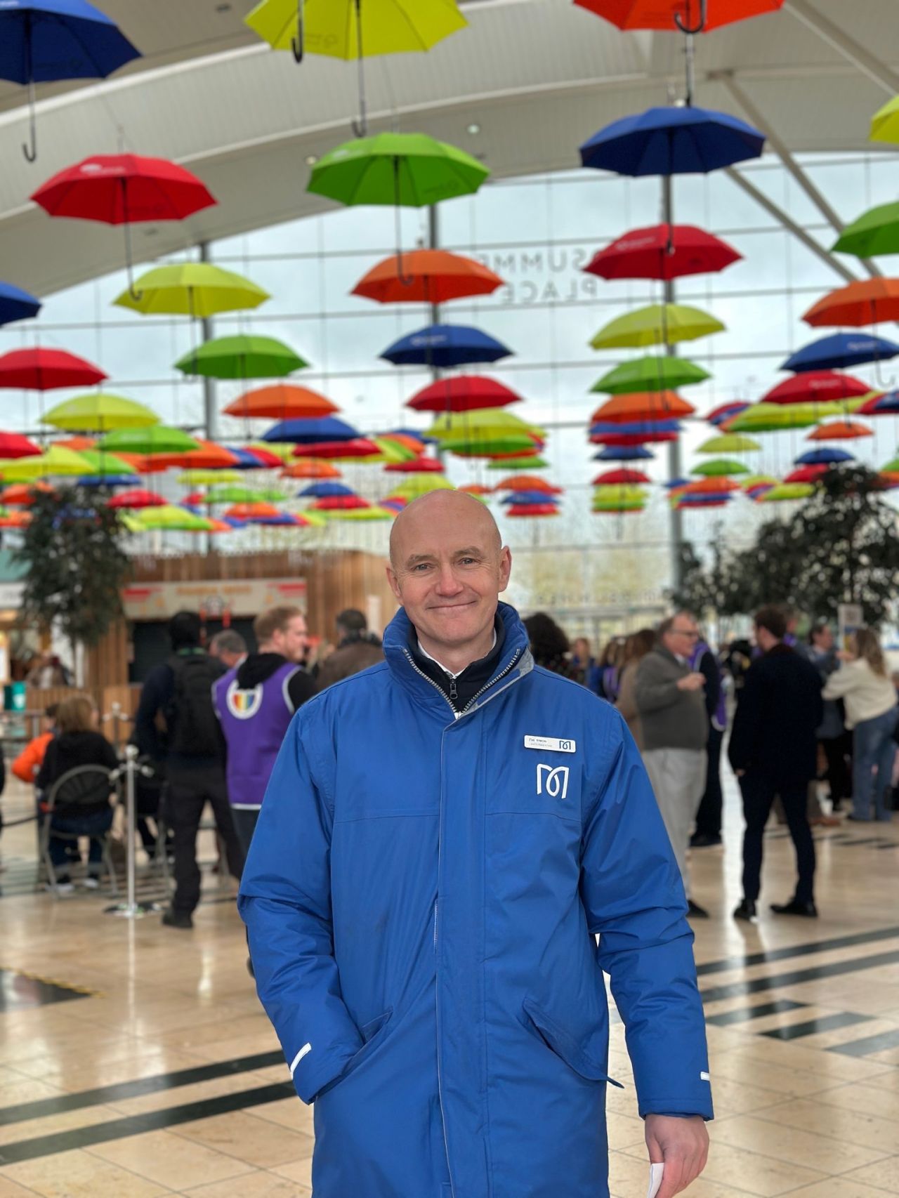 Man smiling underneath a large colourful umbrella display in Milton Keynes